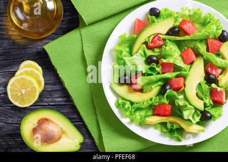 Rote Fische, frisch Salatblätter, Scheiben Avocado und Oliven Salat auf einem weißen Teller am Tisch Matte auf alten, dunklen Holzbrettern mit Olivenöl und Zitrone s Stockfoto