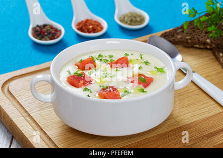 Geräucherter Lachs und Frischkäse Suppe mit Petersilie bestreut in weiße Suppe Tasse auf Schneidebrett mit Löffel, Gewürze, und Vollkorn Roggenbrot mit sunf Stockfoto