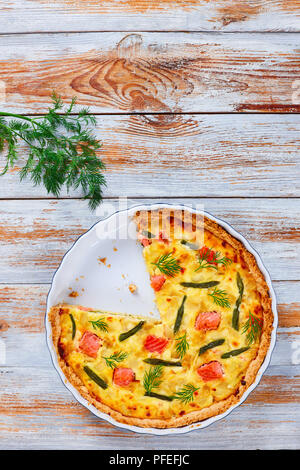 Französische Quiche mit Lachs, grüne Bohnen und Käse, Rahm und Zwiebel in Scheiben geschnitten in der auflaufform auf alten Holztisch mit Haufen frischer Dill auf ol Rost Stockfoto