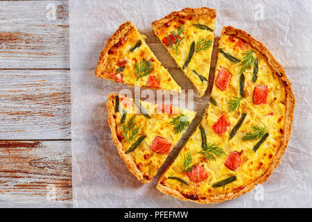 Köstliche hausgemachte französische Quiche mit roten Fischen, grüne Bohne, Soße Béchamelsoße und Emmentaler Käse in Scheiben geschnitten auf Backpapier auf weißem Holz- backgroun Stockfoto