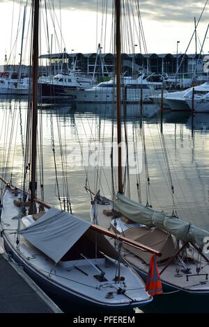 Zwei vintage Segel Boote, Steg in der Marina gebunden in Abend mit großer Energie Boote im Hintergrund. Stockfoto