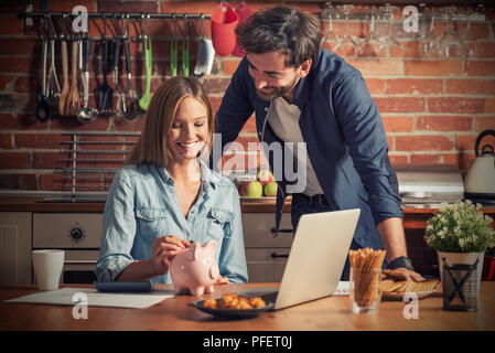 Familie, Haushalt und Finanzen. Junge Frau setzt eine Münze in das Sparschwein. Stockfoto