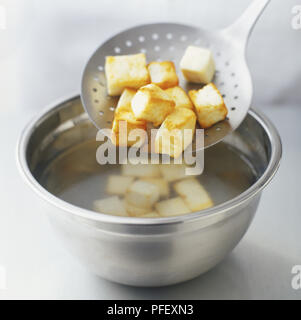 Würfel frittierte paneer Käse spooned aus einer Schüssel mit lauwarmem Wasser, Stockfoto