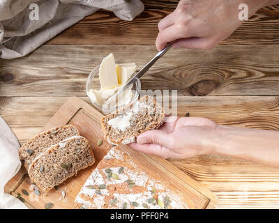 Weibliche Hände ausbreiten Butter auf ein Sandwich. Hausgemachtes Roggenbrot auf einem Holztisch Stockfoto