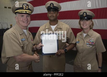 NORFOLK, Virginia (12. Juni 2018) - - Senior Chief's Aviation Bootsmann Mate (Handling) Sean Devereaux, aus Philadelphia, auf USS Gerald R. Ford's (CVN 78) Luft Abteilung zugewiesen, erhält seinen frocking Brief von Kapitän Richard McCormack, Ford's kommandierenden Offizier, und Command Master Chief Laura Nunley, master Befehl Ford's Chief, während ein Senior Chief Petty Officer pinning Zeremonie in den Hangar Bay. Ford hatte 14 Chief Petty Officers in den Rang eines Senior Chief Petty Officer. Stockfoto