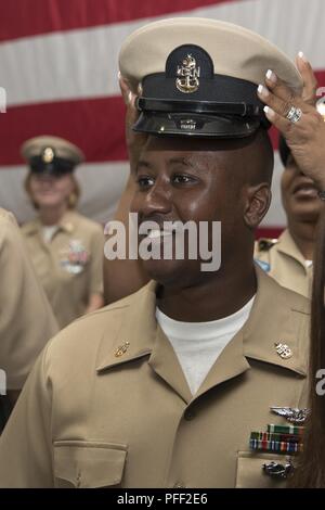 NORFOLK, Virginia (12. Juni 2018) - - Senior Chief Luftfahrt Elektronik Techniker Paul Glenn, aus Atlanta, USS Gerald R. Ford's (CVN 78) Aviation intermediate maintenance Abteilung zugewiesen, wird vom Master Chief Avionik Techniker Tinesha Truppe während eines Senior Chief Petty Officer pinning Zeremonie in den Hangar bay abgedeckt. Ford hatte 14 Chief Petty Officers in den Rang eines Senior Chief Petty Officer. Stockfoto