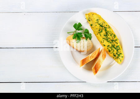 Köstliche basic Französisch Ausschreibung Omelette mit grünen, Baguette Scheiben und frische Petersilie, auf weiße Platte auf weißen Tisch serviert, Ansicht von oben Stockfoto