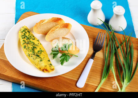 Köstliche französische Ausschreibung Omelette serviert auf weiße Platte mit Baguette Scheiben und frische Petersilie auf Schneidebrett mit Salz- und Pfefferstreuer und Feder Stockfoto