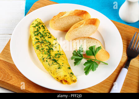 Köstliche basic Französisch Ausschreibung Omelette serviert auf weiße Platte mit Baguette Scheiben und frische Petersilie auf Schneidebrett mit Gabel, close-up Stockfoto