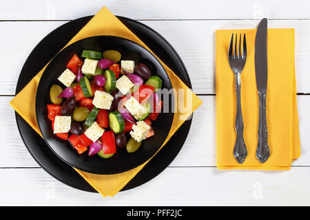 Leckere griechische Salat mit frischem Gemüse, Schafskäse grün und Kalamata Oliven, rote Zwiebel Zwiebeln auf die schwarzen Platten auf Whiteboards mit Gabel und knif Stockfoto