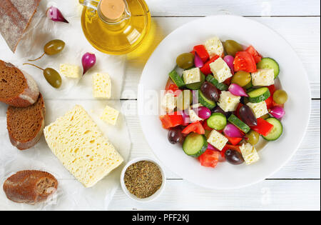 Leckere griechische Salat mit frischem Gemüse, Schafskäse grün und Kalamata Oliven, rote Zwiebel Zwiebeln auf weißen Teller am Tisch mit knusprigem Bauernbrot Stockfoto