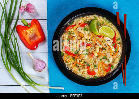 Thai Chicken Nudelsuppe bestreut mit gehackter Cilantro, Sesam und Erdnüsse in schwarz Schüssel mit Stäbchen. grüne Zwiebel, die Hälfte der Red Paprika und g Stockfoto