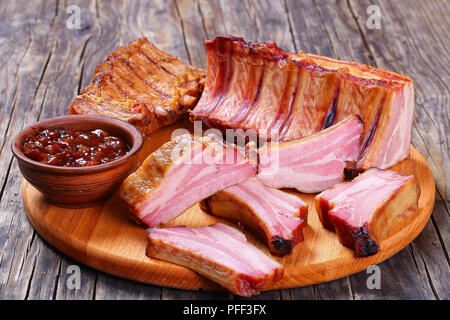 Lecker geräucherten Rippchen und in Scheiben geschnitten mit Barbecue Sauce auf runden Schneidbrett auf dunklen Holztisch, Ansicht von oben, close-up Stockfoto