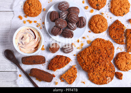 Hausgemachte Schokolade Chip oatmeal Cookies, Rosinen, Kekse, Schokolade, Walnüsse und frischem Joghurt in der Schüssel auf Papier auf Holz- Tabelle, Ansicht von oben Stockfoto