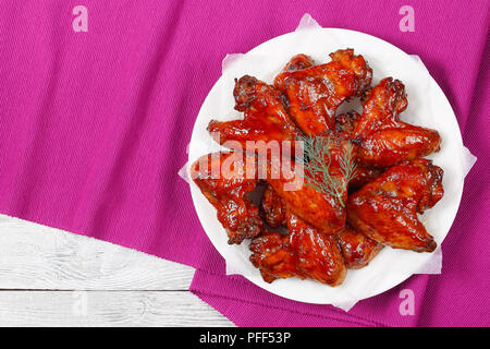 Lecker knusprig gebratener Honig Sriracha Chicken Wings auf weiße Platte, auf Holztisch, einfaches Rezept, von oben betrachten Stockfoto