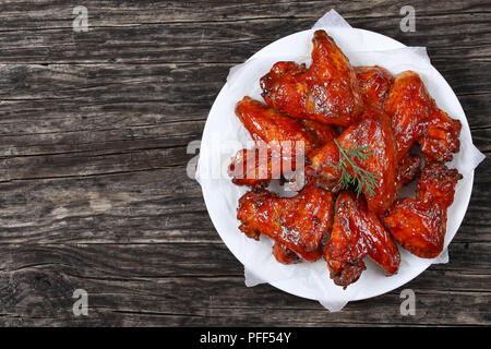 Lecker knusprig gebratene Hühnerflügel auf Platte auf dunklen Holz- Tabelle, Ansicht von oben Stockfoto