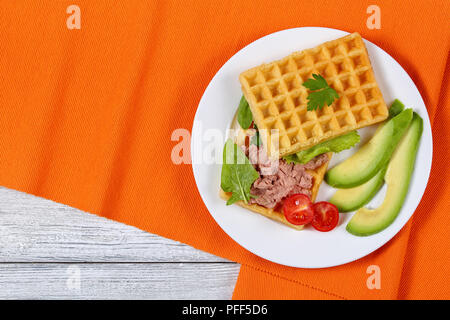 Leckere gesalzene belgische Waffeln Sandwich mit Avocado, Scheiben, Türkei Leber Pate, Salat, Spinat und die Petersilie auf weiße Platte mit Kirschtomaten, er Stockfoto