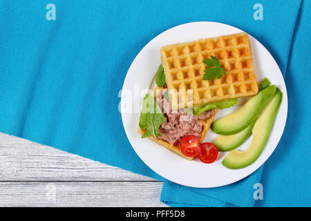 Leckere gesalzene belgische Waffeln Sandwich mit Avocado, Scheiben, Türkei Leber Pate, Salat, Spinat und die Petersilie auf weiße Platte mit Kirschtomaten, er Stockfoto