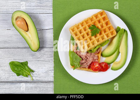 Leckere gesalzene belgische Waffeln Sandwich mit Avocado, Scheiben, Türkei Leber Pate, Salat, Spinat, Tomaten und Petersilie auf weiße Platte, halb o Stockfoto