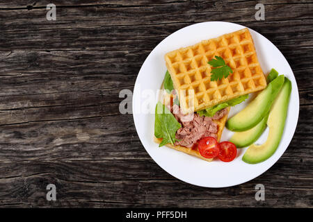 Leckere gesalzene belgische Waffeln Sandwich mit Avocado, Scheiben, Türkei Leber Pate, Salat, Spinat, Tomaten und Petersilie auf weiße Platte auf dunklen Stockfoto
