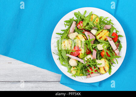 Köstliche gegrillte Zucchini, Mozzarella, Käse, Fleisch, Tomaten und Rucola Sommer Salat auf weißen Teller am Tisch Matte, Ansicht von oben Stockfoto