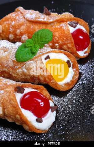 Leckere sizilianische Cannoli, traditionelle italienische Dessert, Füllung mit ricotta Käse und cocktailkirschen auf schwarze Platte auf dunklem Schiefer Fach, authentische cl Stockfoto