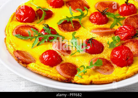 Leckere Omelette mit Würstchen in Scheiben schneiden, Kirschtomaten und frische Rucola auf weißem Platter, Ansicht von oben, close-up Stockfoto