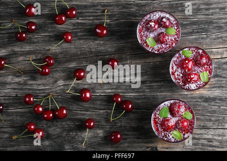 Lecker kalten Sommer Nachtisch, Sweet cherry Jelly in drei Glas Tassen mit Kokos Chips dekoriert Glasur mit Minze auf dunklen alten Tisch mit ch Stockfoto
