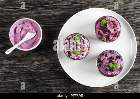 Leckeren, gesunden Sommer dessert Schwarze Johannisbeeren mit Minze im Glas Tassen auf Platte eingerichtet. Gefrorene Creme ricotta Joghurt Mousse in Schüssel Schlagsahne Stockfoto