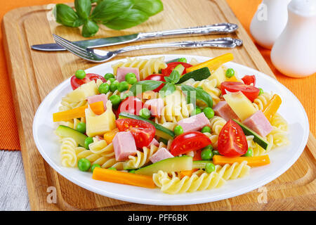 Licht fröhlich bunte Antipasti Salat von italienischer Pasta Fusilli mit Karotten und Zucchini Sticks, Schinken, Käse, Erbsen, Tomaten auf weißem Pla Stockfoto