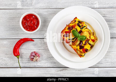 Köstliches Stück Zucchini, rote Bohne, Schinken und Käse Auflauf auf zwei weiße Platten auf Holztisch mit Tomatensauce in Soße Boot serviert, Ansicht von Stockfoto
