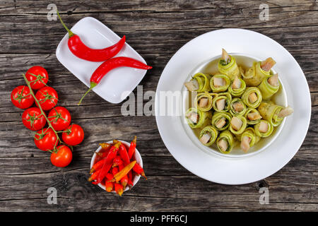 Party Set - Leckere rohe pikante Zucchini rollen Füllen mit Hering, Scheiben, frischen Tomaten und eingelegte Paprika auf Platte auf dunklen Holztisch, vi Stockfoto