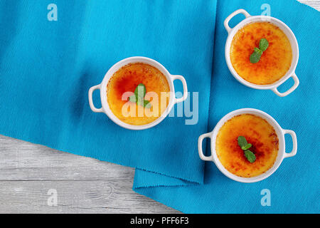 Leckere Crème brûlée oder Trinity Creme mit harten Karamell oben, mit Minze aus weisser Keramik Förmchen auf blauer Tisch Matte, authentische Rezept eingerichtet, v Stockfoto