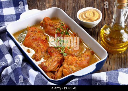 Leckeres geschmortes Kaninchen in Senfsauce in Auflaufform mit einer Flasche Olivenöl auf Holztisch, authentische Rezept, close-up Stockfoto