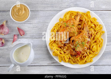 Köstliches Kaninchen in Dijon Senf, Weißwein und Sahne sauce Fettuccine auf weiße Platte mit Zutaten auf hölzernen Tisch serviert, gekocht, verbindlich Stockfoto