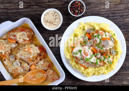 Leckere Stücke von Kaninchen geschmort in der sauren Sahne mit Pilzen und Karotten mit Kartoffelbrei, serviert mit Petersilie auf weiße Platte auf dunklen sprengte Stockfoto