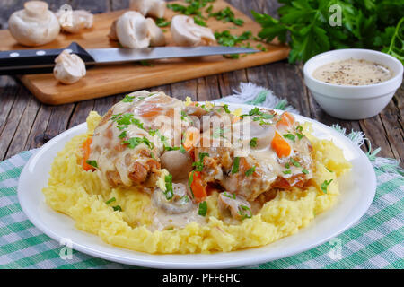 Stücke von Kaninchen geschmort in saurer Sahne Sauce mit Pilzen und Karotten mit Kartoffelbrei, serviert mit Petersilie auf weiße Platte schneiden Wildschwein sprengte Stockfoto