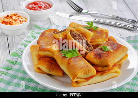 Aufgerollt köstliche Crêpes mit Hackfleisch/Leber und Fleisch auf weiße Platte auf alten Holztisch mit sauceon Hintergrund Blick von oben, in der Nähe gefüllt - Bis Stockfoto