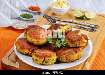 Köstliche frisch gebratenen Fisch, hausgemachte Kuchen auf weiße Platte auf Schneidebrett mit Gabel, Messer, Soße und Gewürze, authentische Rezept, Ansicht von oben, in der Nähe Stockfoto