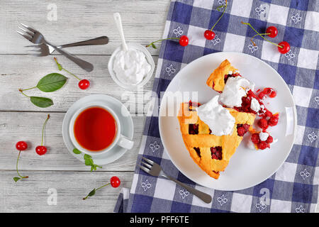 Scheiben köstliche hausgemachte Sour Cherry Pie an der Platte. Schüssel mit Schlagsahne, Dessert gabeln, Tasse Tee auf Küche Tuch, klassisches Rezept, Ansicht von Stockfoto