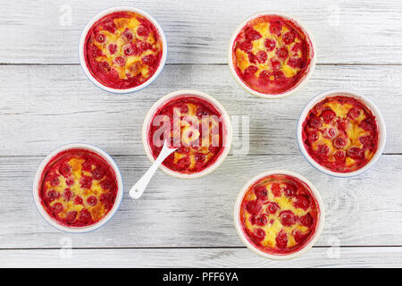 Leckere Sour Cherry clafoutis - klassische französische süße Frucht Vanille hausgemachten Dessert in Keramik Förmchen mit Löffel auf Holztisch, authentische Rezept, Stockfoto