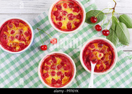 Leckere Sour Cherry clafoutis - klassische französische süße Frucht Vanille hausgemachten Dessert in Keramik Förmchen mit Löffel auf Küche Tuch auf Holztisch, Stockfoto