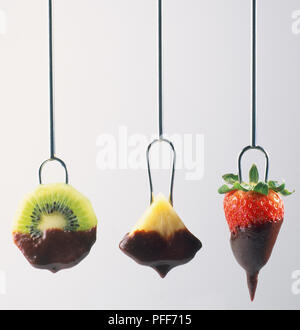 Drei Stücke Obst, Kiwi, Ananas, Erdbeere, auf die Gabeln in Schokolade getauchten Sauce Stockfoto