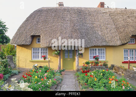 Republik von Irland, County Limerick Adare, Reetdachhaus mit gelben Wänden und Blume Garten vor. Stockfoto