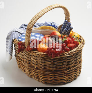 Einen Weidenkorb mit frischem Obst, Besteck, Geschirrtuch und Platten Stockfoto