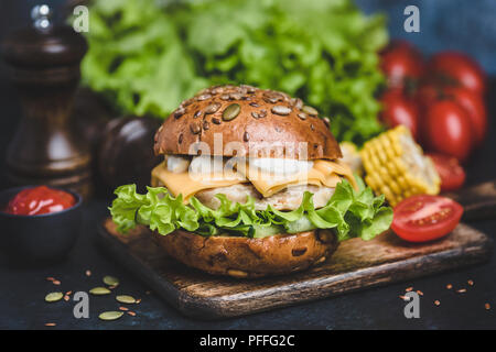 Leckere Chicken Burger auf Holz serviert. Cheeseburger mit Käse, weiße Soße, Salat, Tomaten. Detailansicht, selektiver Fokus Stockfoto