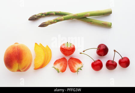 Pfirsich, ganz und geschnitten, Erdbeere, ganz und halbiert, vier Kirschen und zwei Halme von grünem Spargel Stockfoto