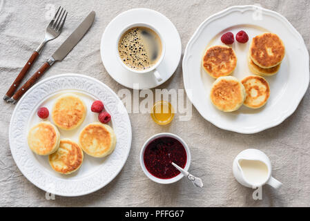 Frühstück Tabelle Quark Pfannkuchen, Kaffee, Sahne, Honig und Marmelade. Background. Leckeres Frühstück, Syrniki. Russische Küche Stockfoto