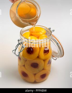 Gießen Sirup über Pfirsichen und Kirschen im Glas, close-up Stockfoto