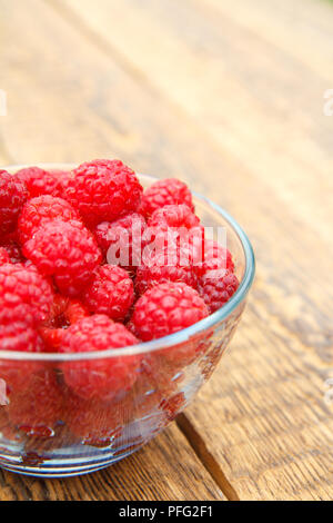 Nahaufnahme reife Himbeeren in die Glasschale auf Holzplatten. Frische Beeren im Garten abgeholt Stockfoto